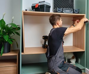 Man measuring wooden cabinet, using measuring tape and pencil to mark panel during home furniture assembly